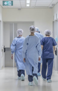 Vier Ärzte von hinten laufen in OP Bekleidung den Flur entlang